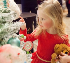 Sweet little girl touches a cupcake ornament on a Christmas tree.