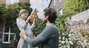 Father and daughter in garden of their home with house model